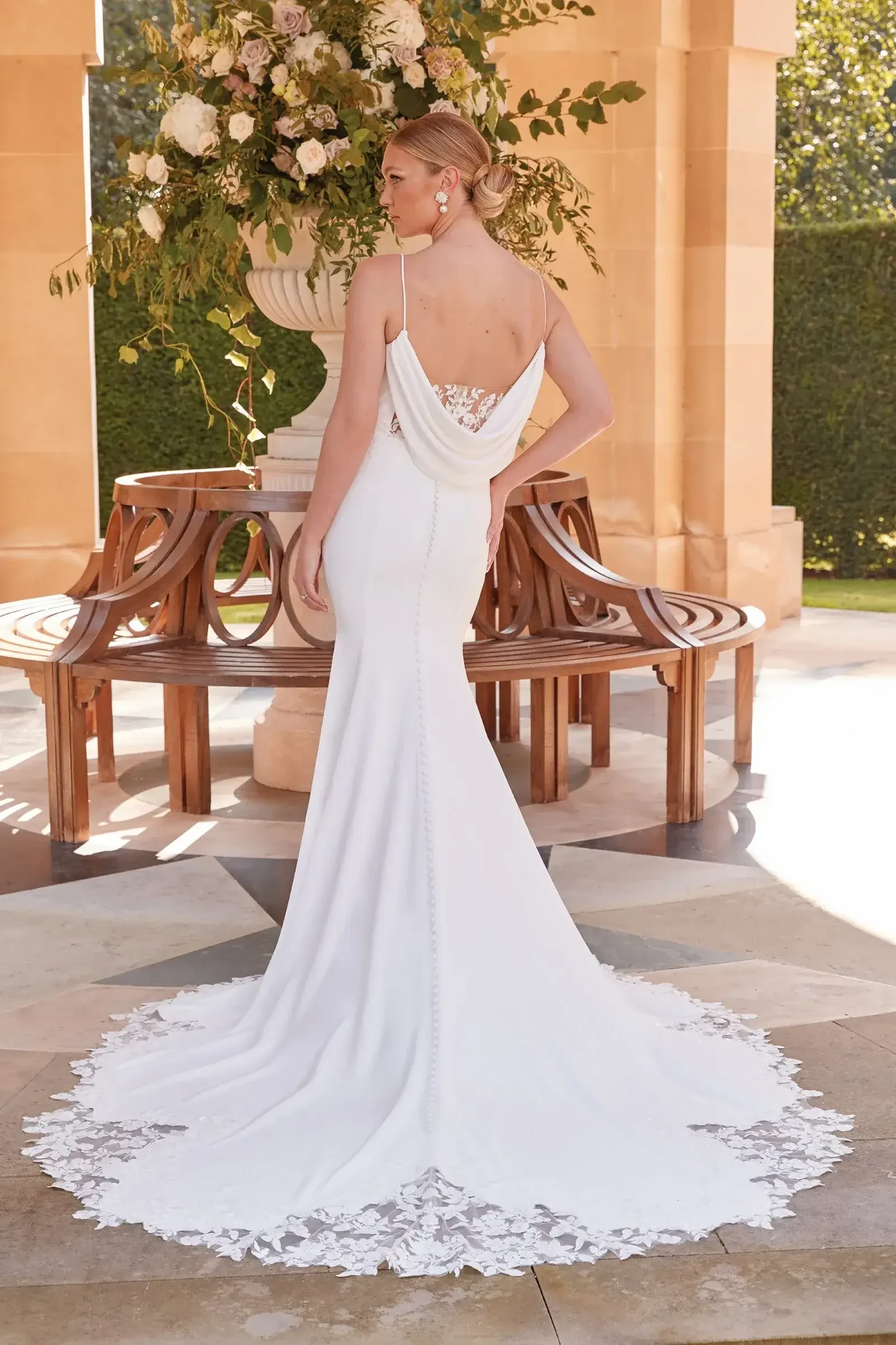 Model is wearing a minimalist cowl back wedding dress with lace cutout train and delicate straps