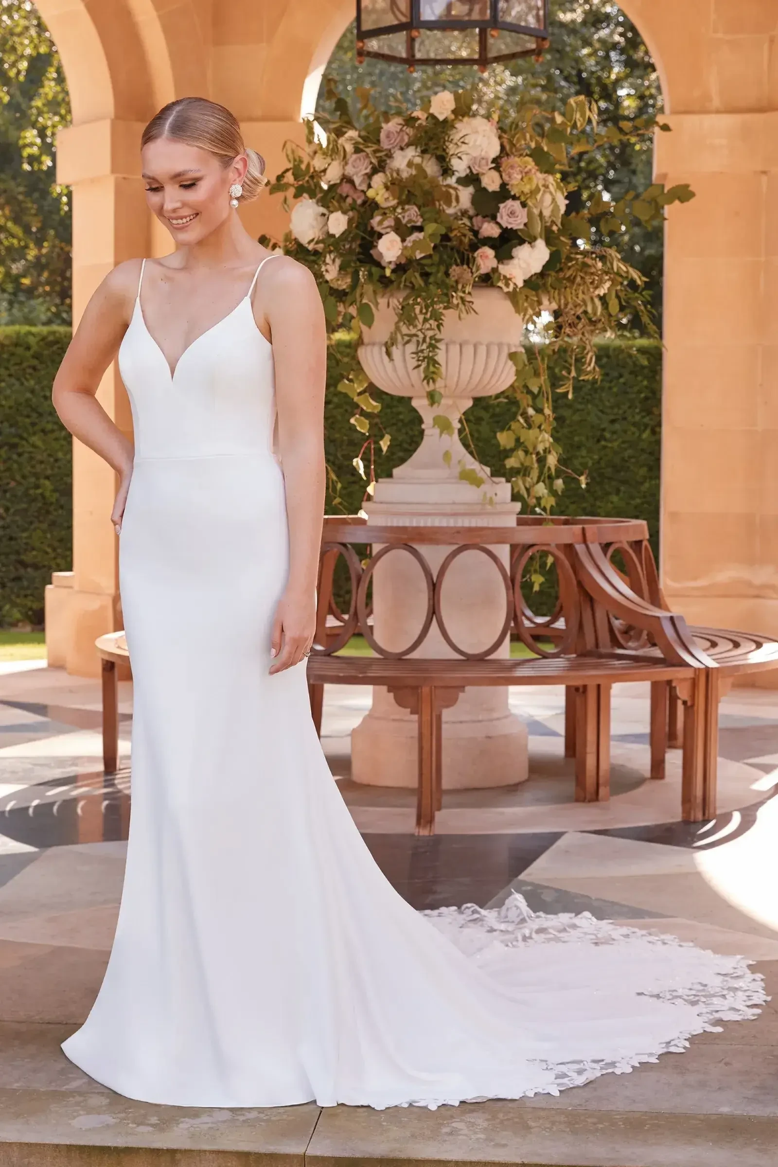 Model is wearing a minimalist cowl back wedding dress with lace cutout train and delicate straps