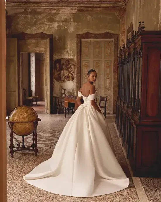 Model is wearing a mikado ball gown wedding dress with a ruched bodice and basque waistline.