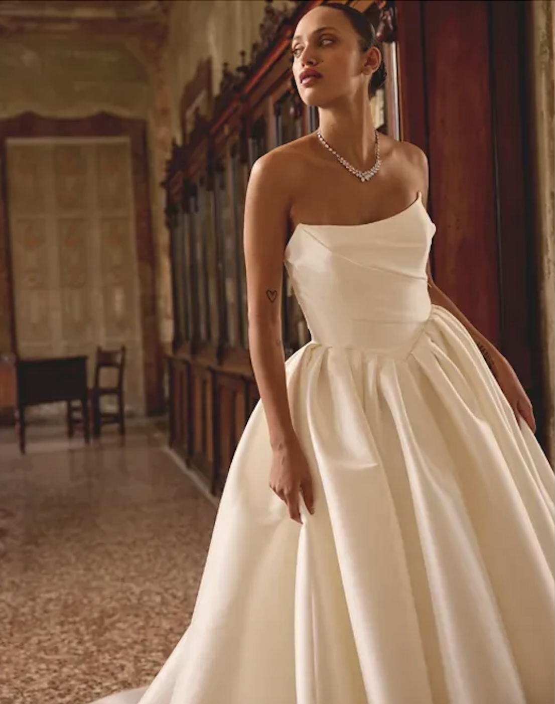 Model is wearing a mikado ball gown wedding dress with a ruched bodice and basque waistline.