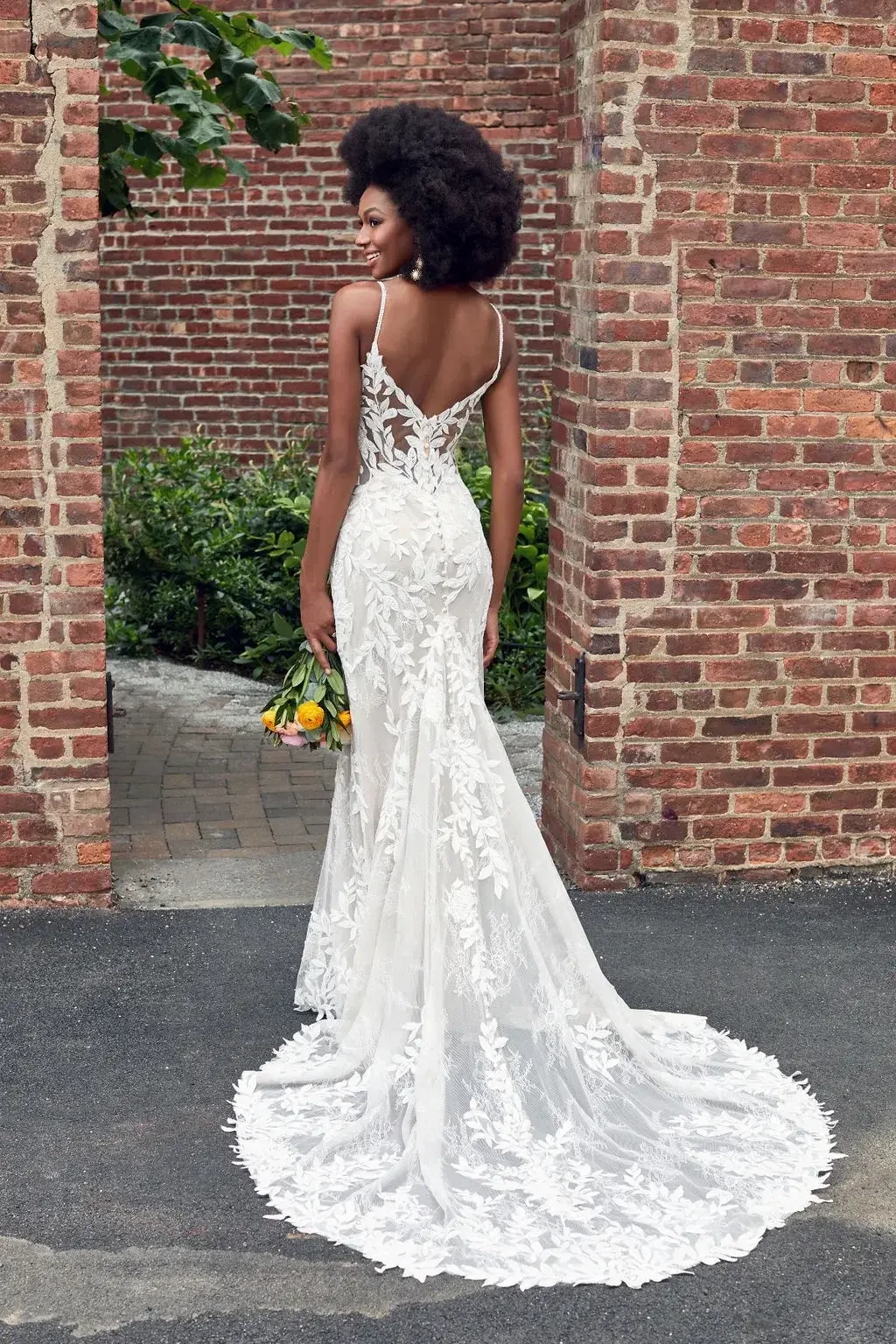 Model is wearing a lace sleeveless wedding dress with a train