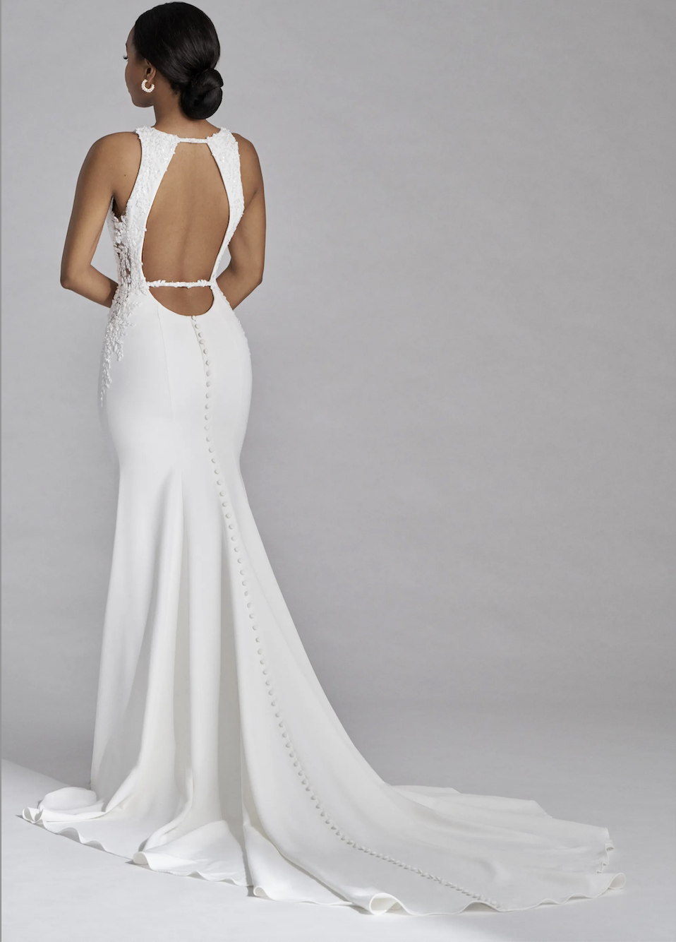 Model is wearing a sleeveless high neck wedding dress with a keyhole back